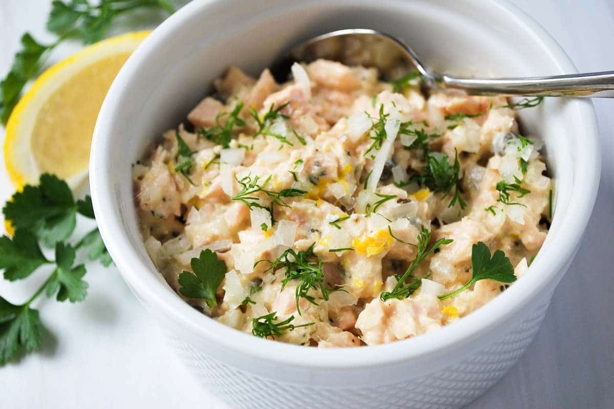 Mediterranean tuna salad in a white bowl with fresh herbs and a lemon slice