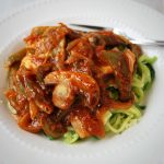 Close up photo of chicken with a tomato, pepper, and mushroom red sauce over zucchini noodles in a bowl