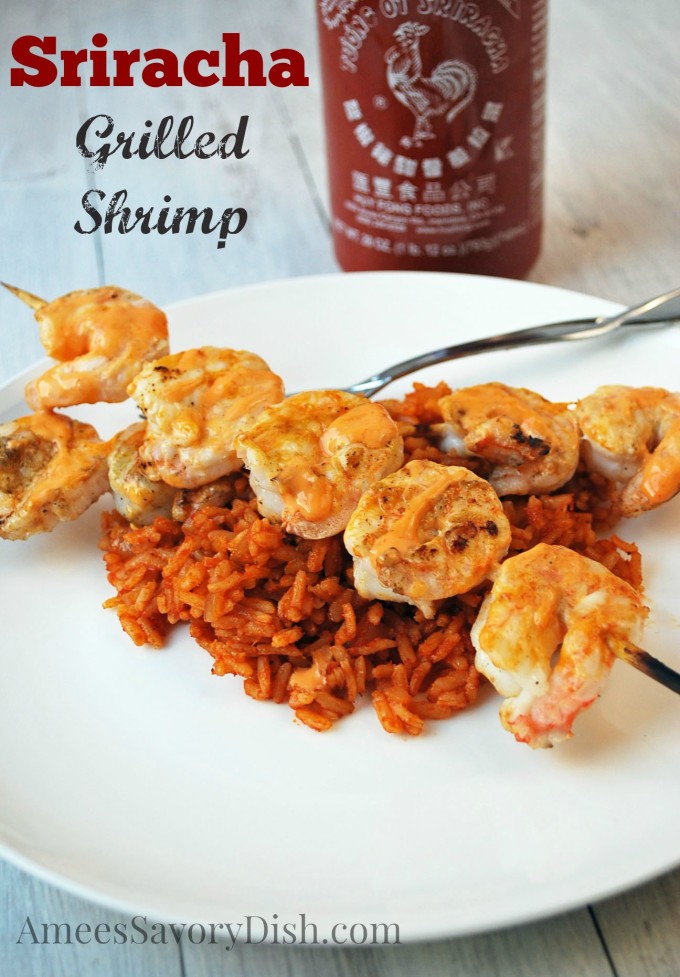 two grilled shrimp skewers over rice rice with a bottle of Sriracha sauce in the background