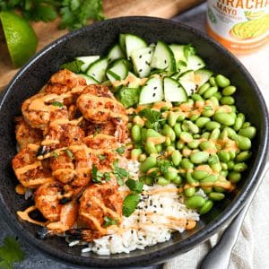 close up of a shrimp and rice bowl with cucumber, edamame, grilled shrimp, rice, cilantro, and drizzled with sriracha mayo