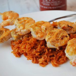 grilled shrimp on skewers over red rice drizzled with Sriracha sauce