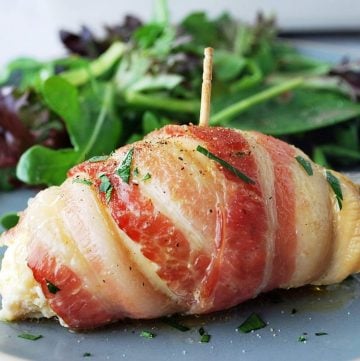 close up of a bacon-wrapped chicken breast sprinkled with fresh parsley on a plate with greens