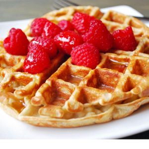 Belgian protein waffle on a plate with raspberries and syrup
