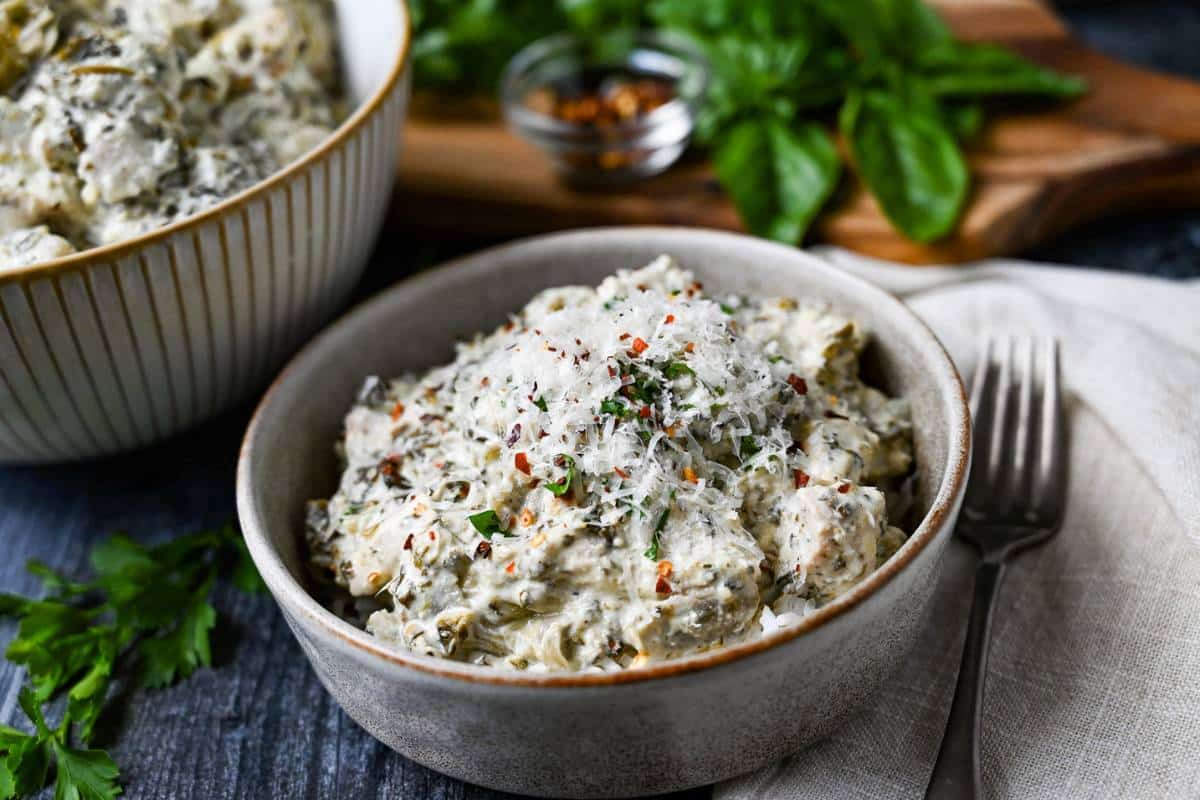 a bowl of creamy chicken with parm on top with a napkin and fork