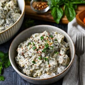 a centered bowl of artichoke spinach chicken with fresh basil and red pepper flakes