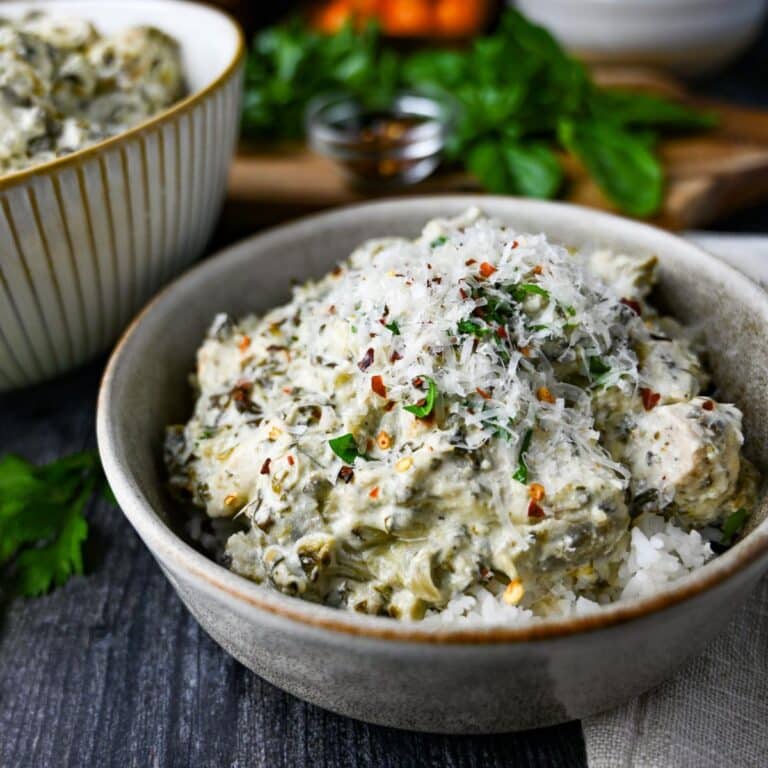 chicken with spinach and artichokes cooked in a slow cooker in a bowl with garnishes