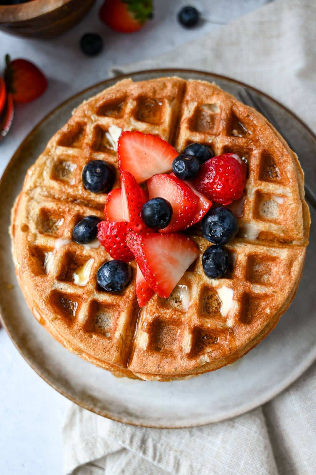 a waffle on a plate with a napkin upderneath with berries on top