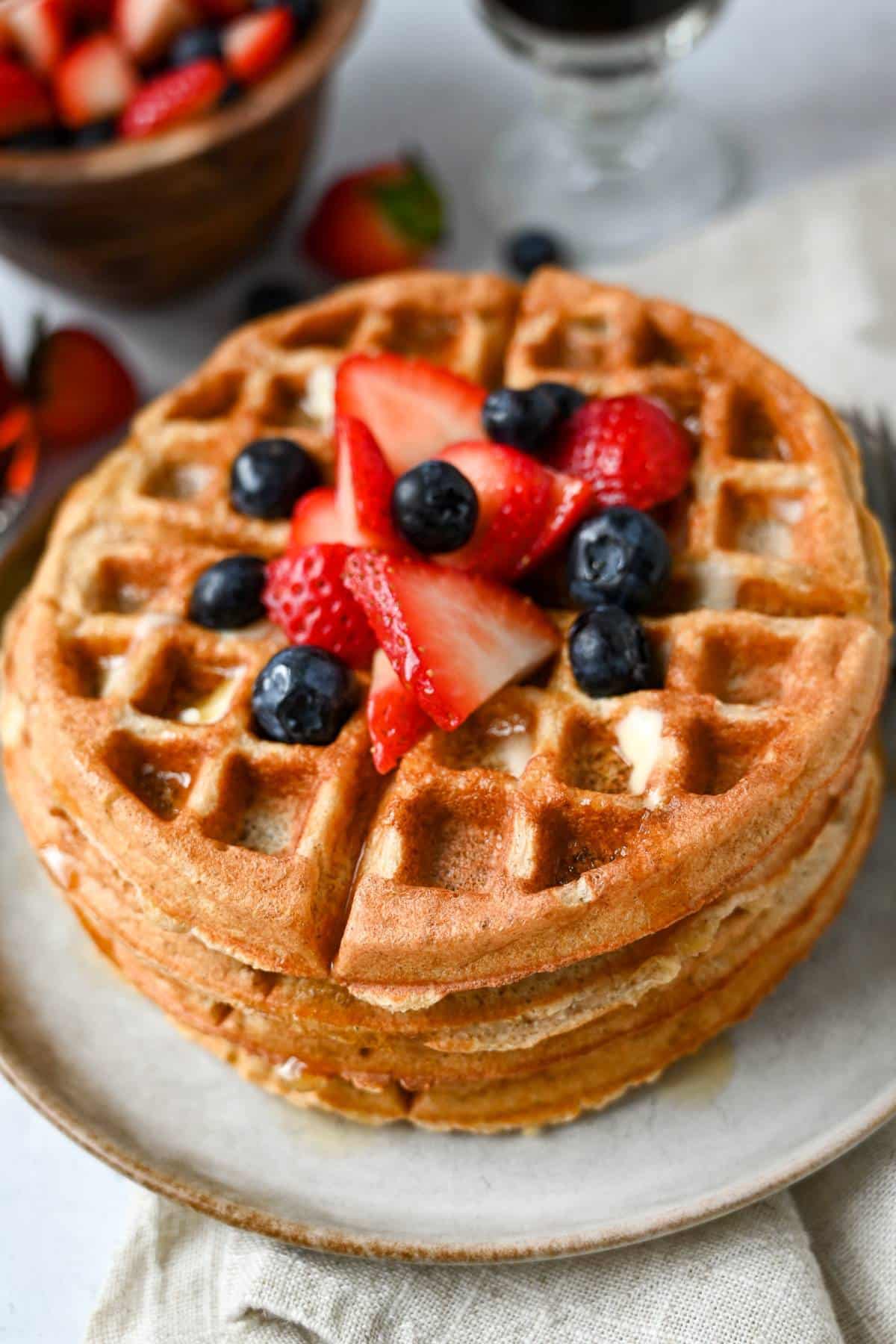 side view of a stack of waffles with berries and syrup