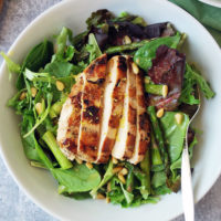 Sliced grilled chicken on top of a salad in a bowl with a fork