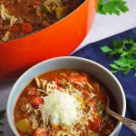 bowl of lasagna soup with pot of soup in the background and fresh herbs