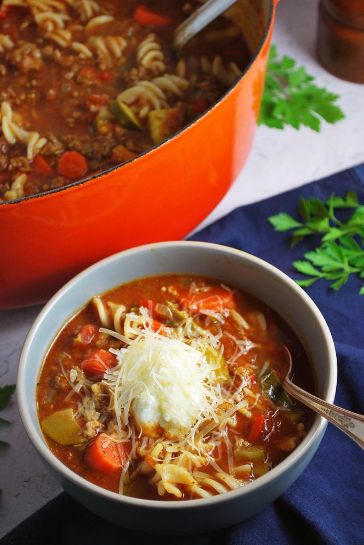 bowl of lasagna soup with pot of soup in the background and fresh herbs