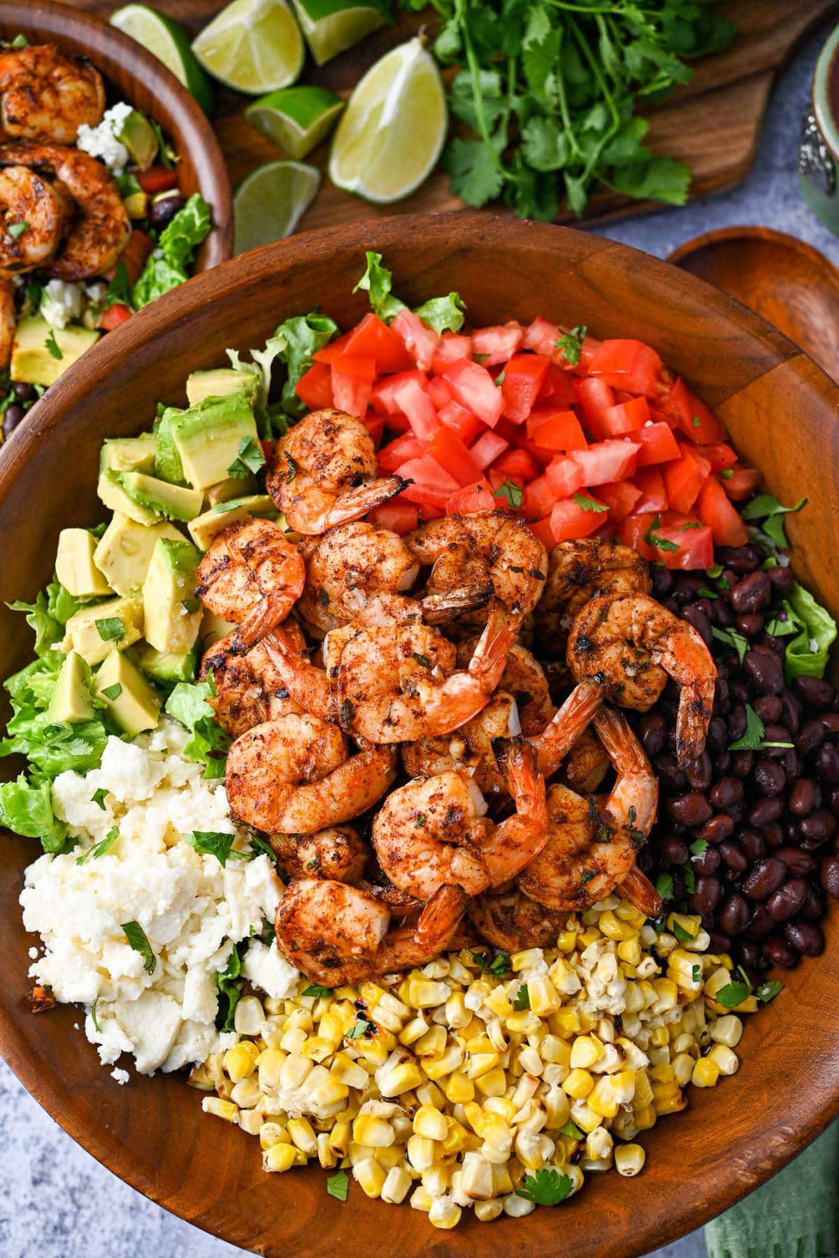 loaded grilled shrimp salad with tomatoes, avocado, beans, cheese, and grilled corn in a large wood bowl