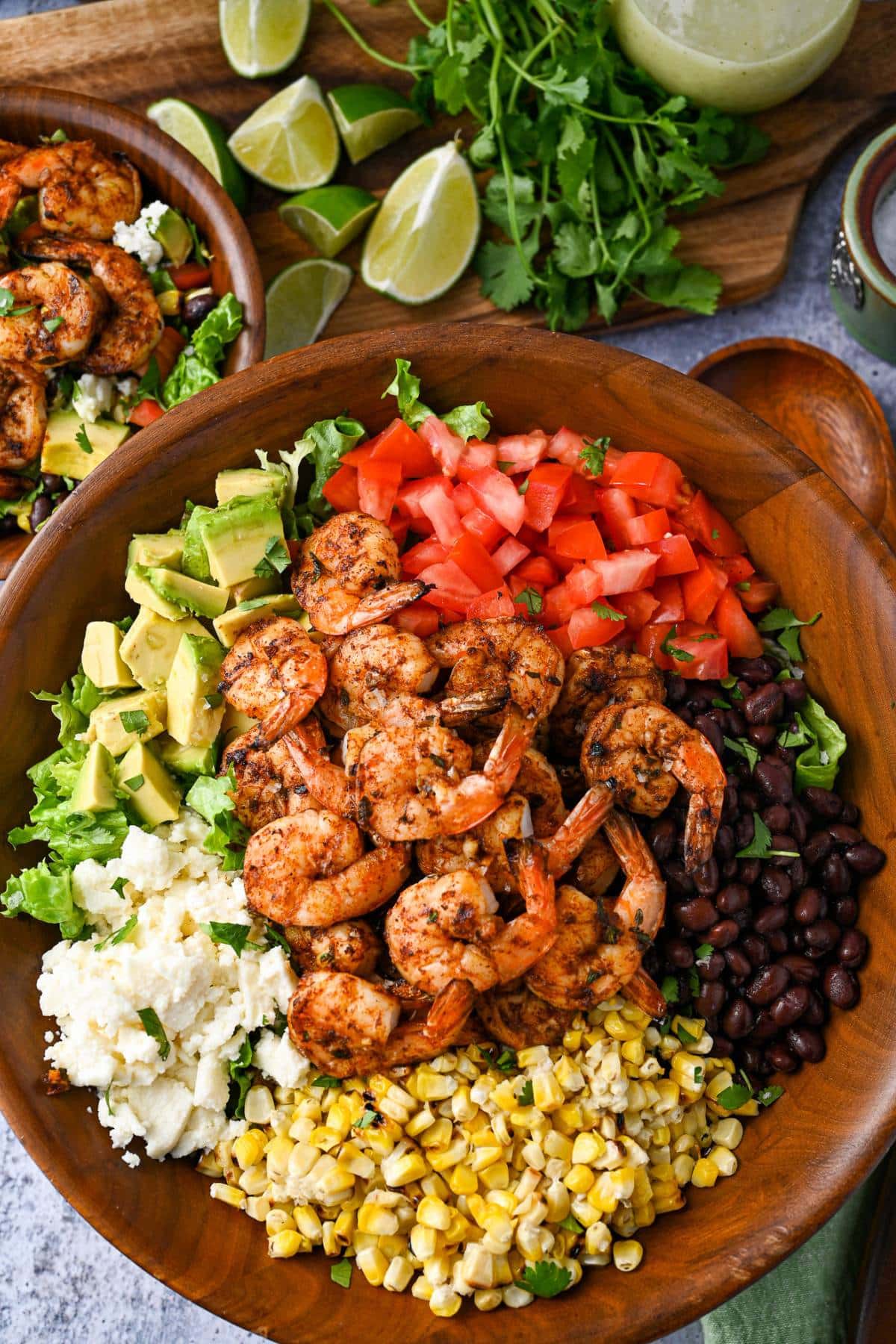 overhead photo of a loaded grilled shrimp taco salad with lime wedges, cilantro, dressing, and a bowl of salad on the side