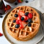 a stack of waffles on a plate surrounded by berries with berries on top