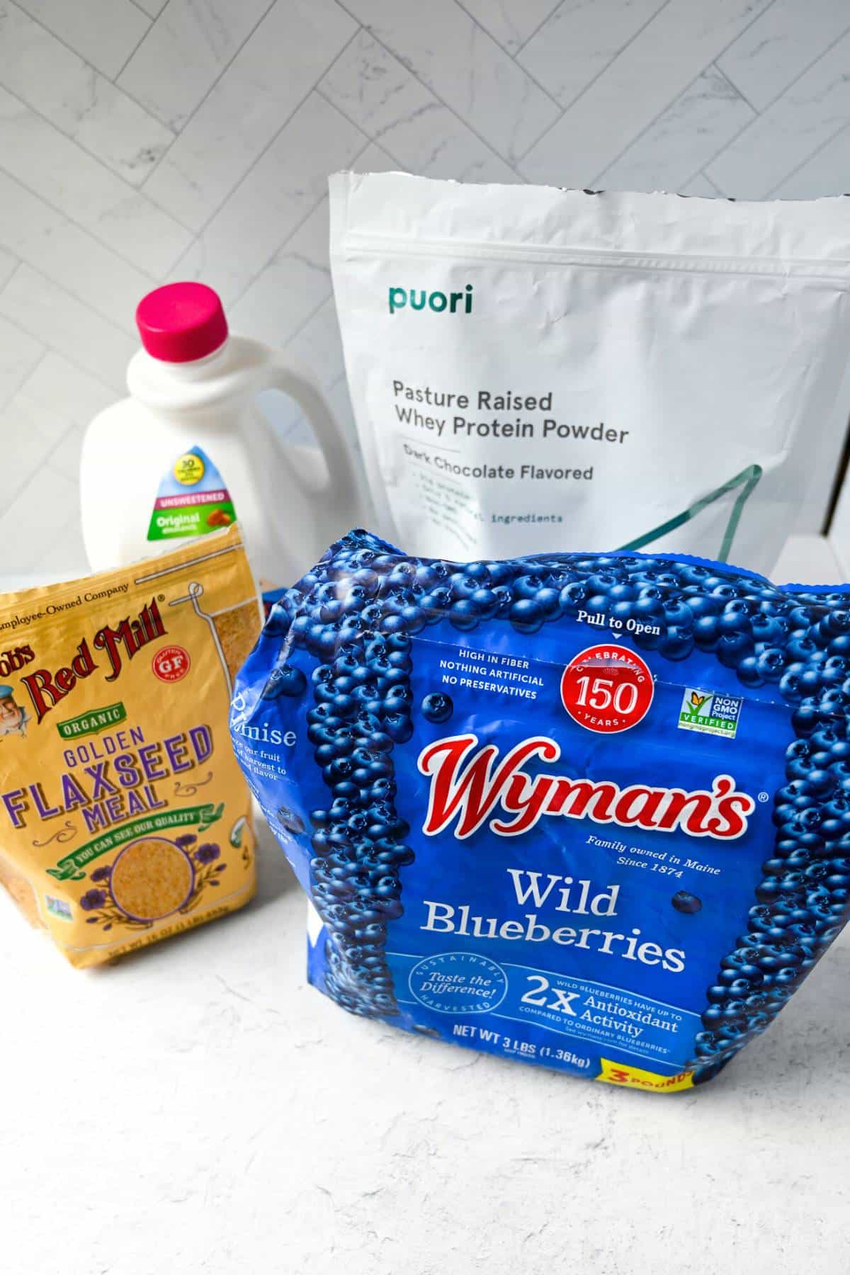 ingredients for making a blueberry protein shake: milk, wild blueberries, protein powder, and flaxseed
