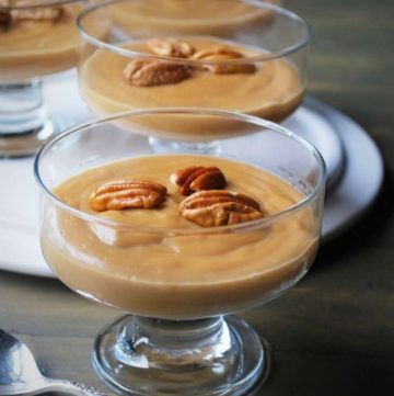 close up of butterscotch pudding topped with whole pecans in a parfait glass