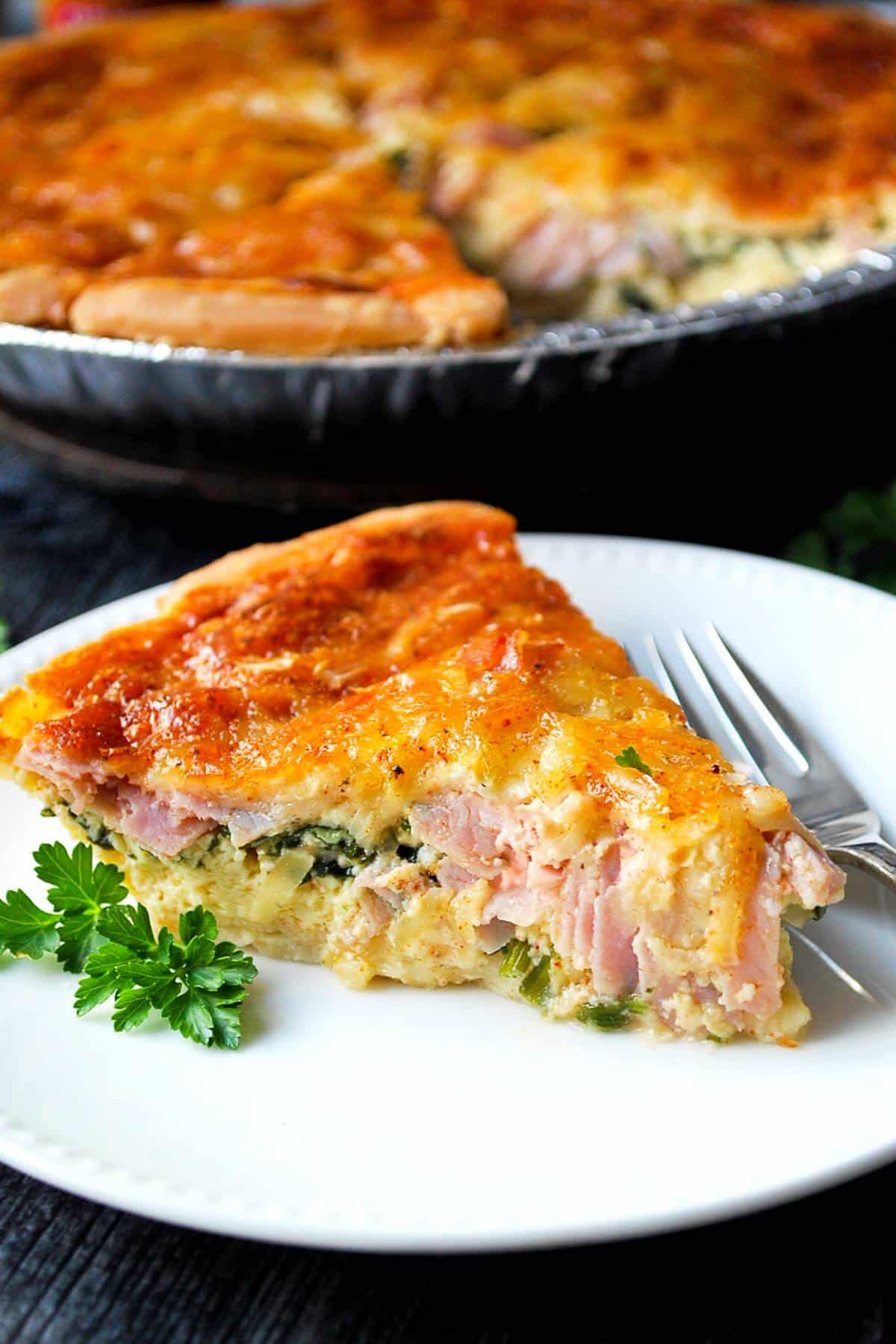 a quiche with a serving sliced out and plated with a fork