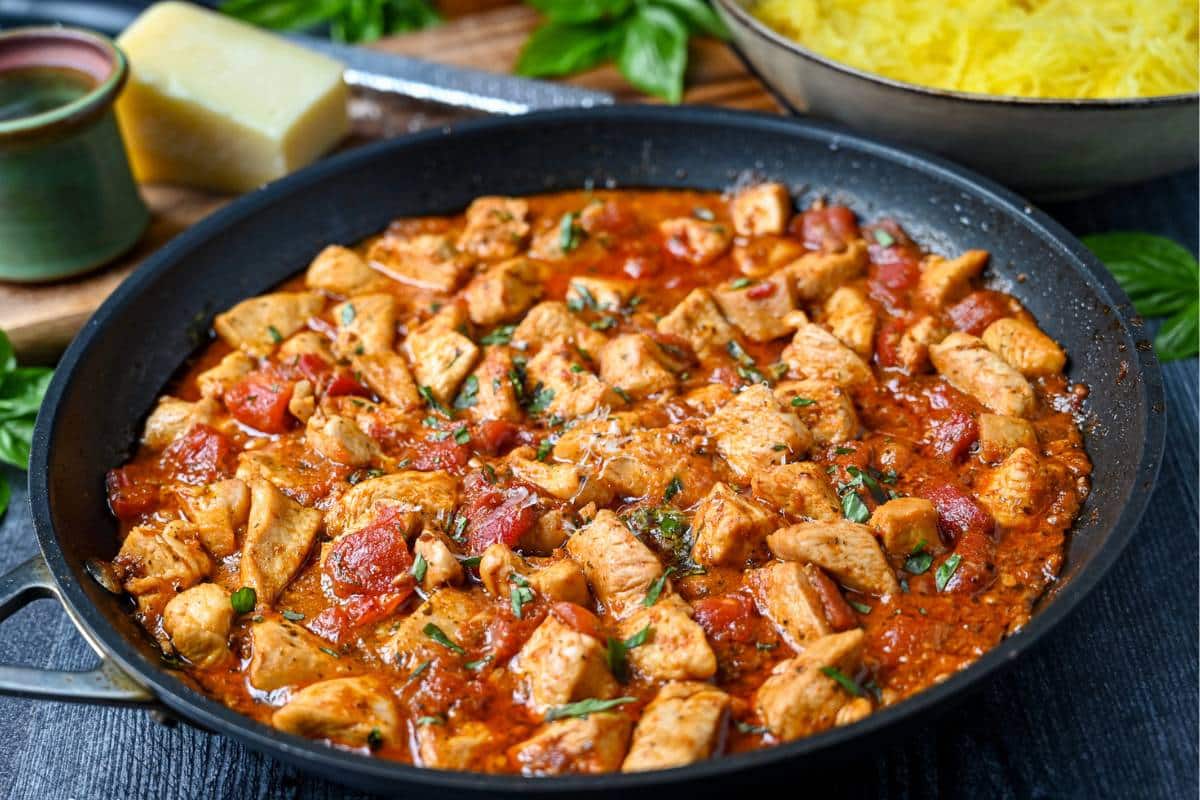 side view of a skillet of cubed chicken breast in a rich sundried tomato pesto sauce with fresh basil