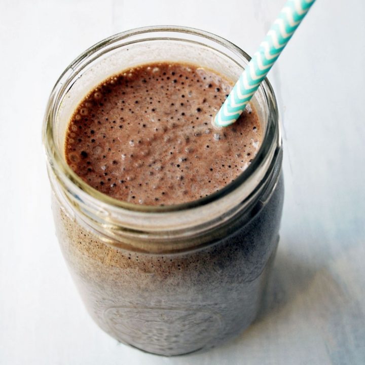 close up photo of blueberry chocolate protein shake with straw in a mason jar