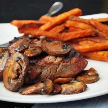 grilled steak on a plate topped with sauteed mushrooms with a side of sweet potato fries