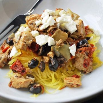 chicken with sun-dried tomatoes, olives, feta cheese and artichokes over a bed of cooked spaghetti squash in a bowl with a fork