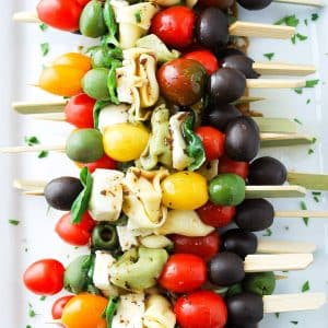 overhead photo of a caprese tortellini skewers drizzled with dressing on a white platter