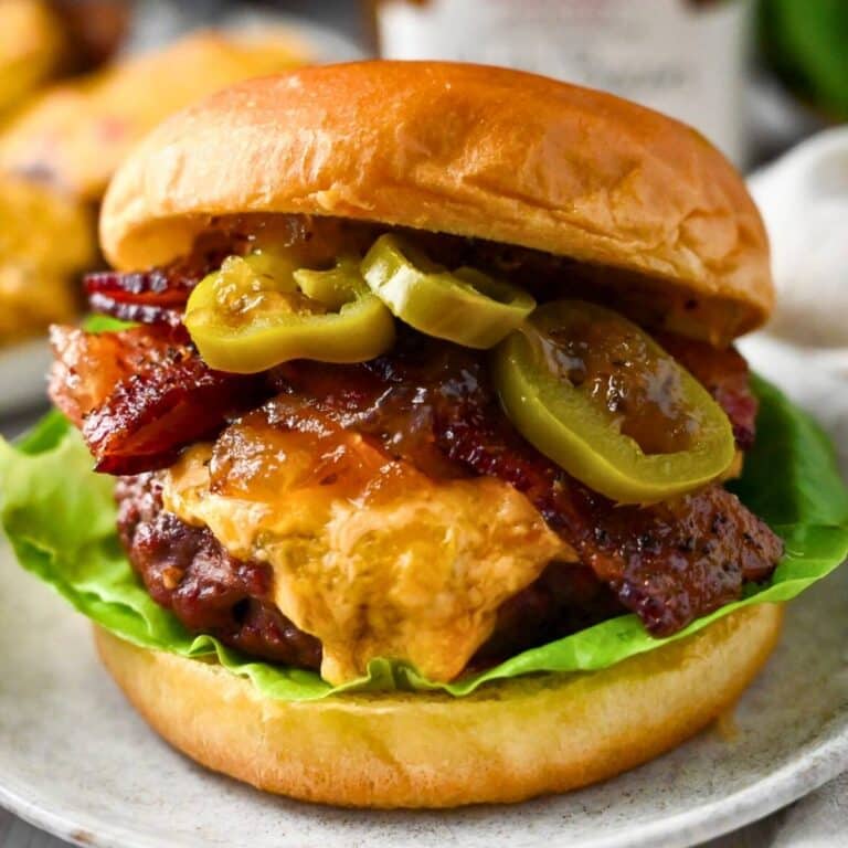 close up of a burger dripping with melted pimento cheese on a bun with bacon, jalapenos, and maple bacon jam