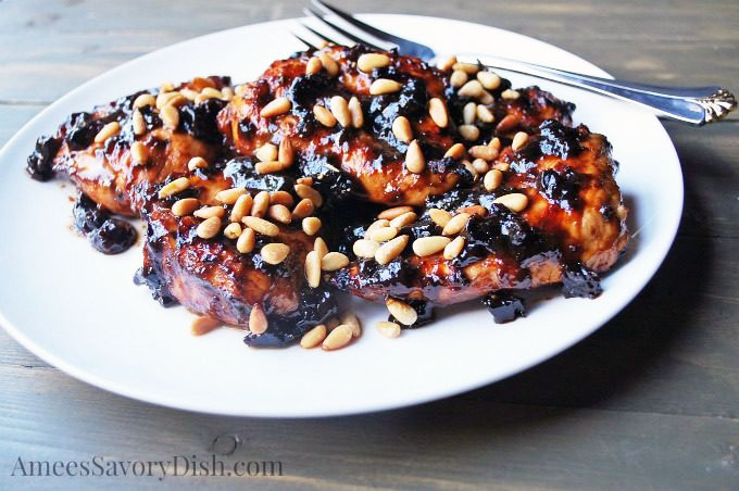 A platter of grilled chicken breasts with a plum glaze and pine nuts