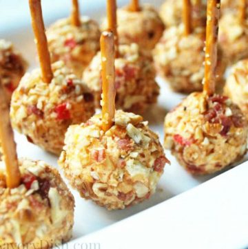 pimento cheese balls covered in crushed nuts on a platter with a pretzel stick stuck in the top for holding