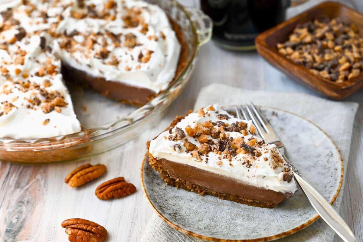 a sliced chocolate toffee cream pie with a bowl of pecans