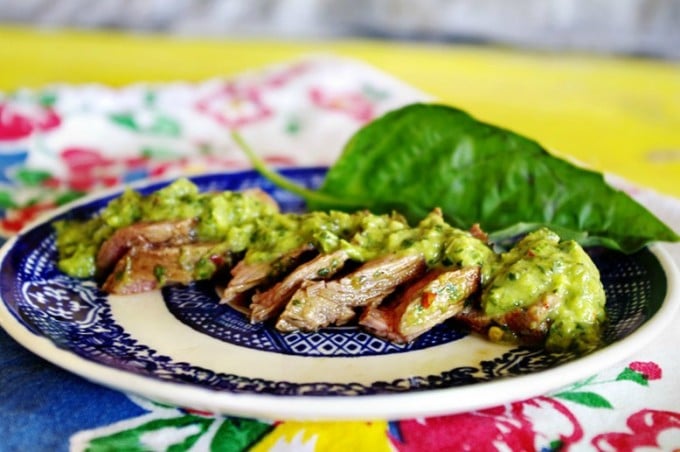 Sliced flank steak topped with chimichurri on a colorful plate