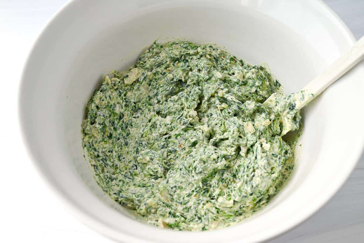 spinach dip mixed in a white bowl with a spatula