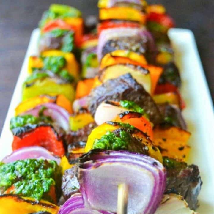 close up of beef skewers with green chimichurri on top