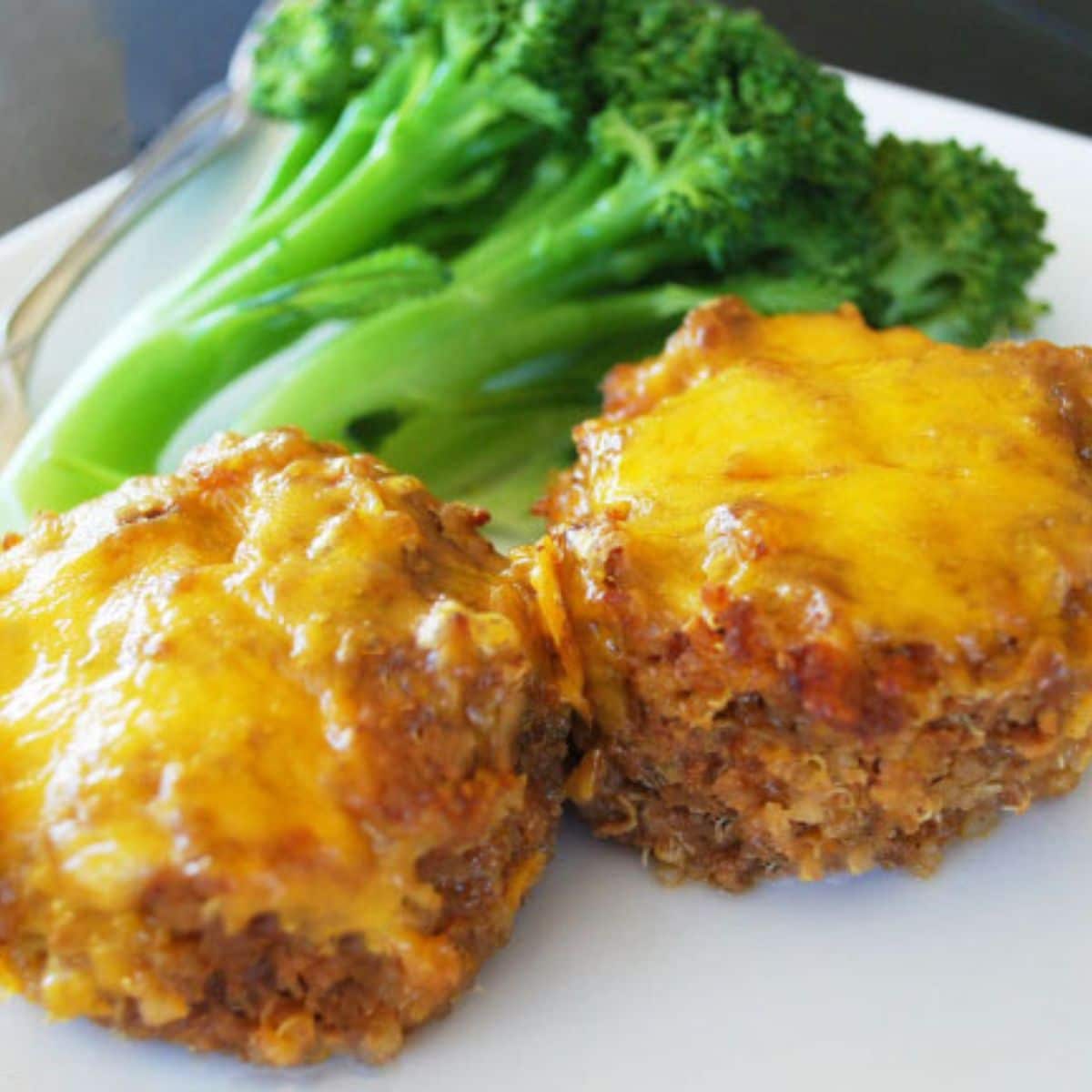 meatloaf muffin topped with melted cheese on a plate with broccoli