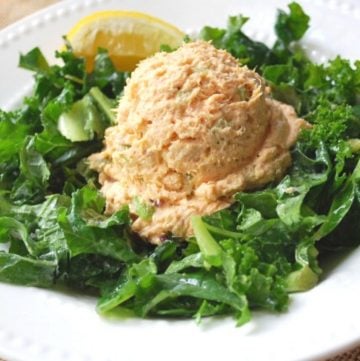 a large scoop of tuna salad on top of kale greens with a slice of lemon in a bowl