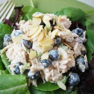 chicken salad with blueberries and almonds on a bed of greens in a bowl