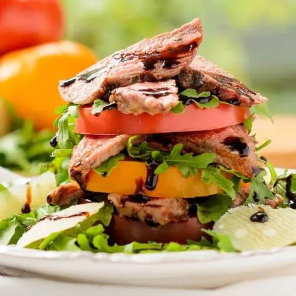 a stacked tomato salad with steak and arugula