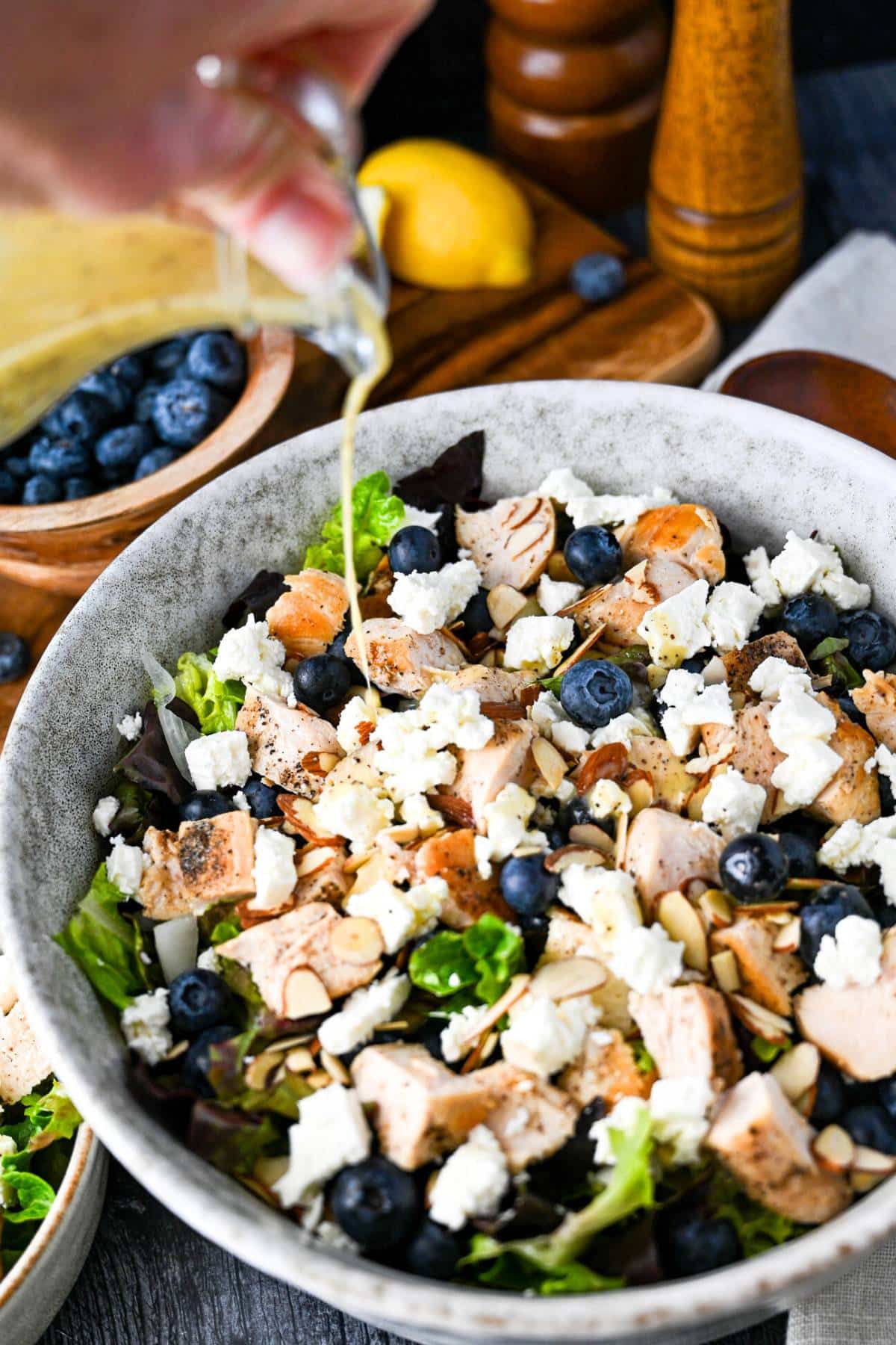 pouring dressing onto a bowl of chopped chicken blueberry and feta salad 