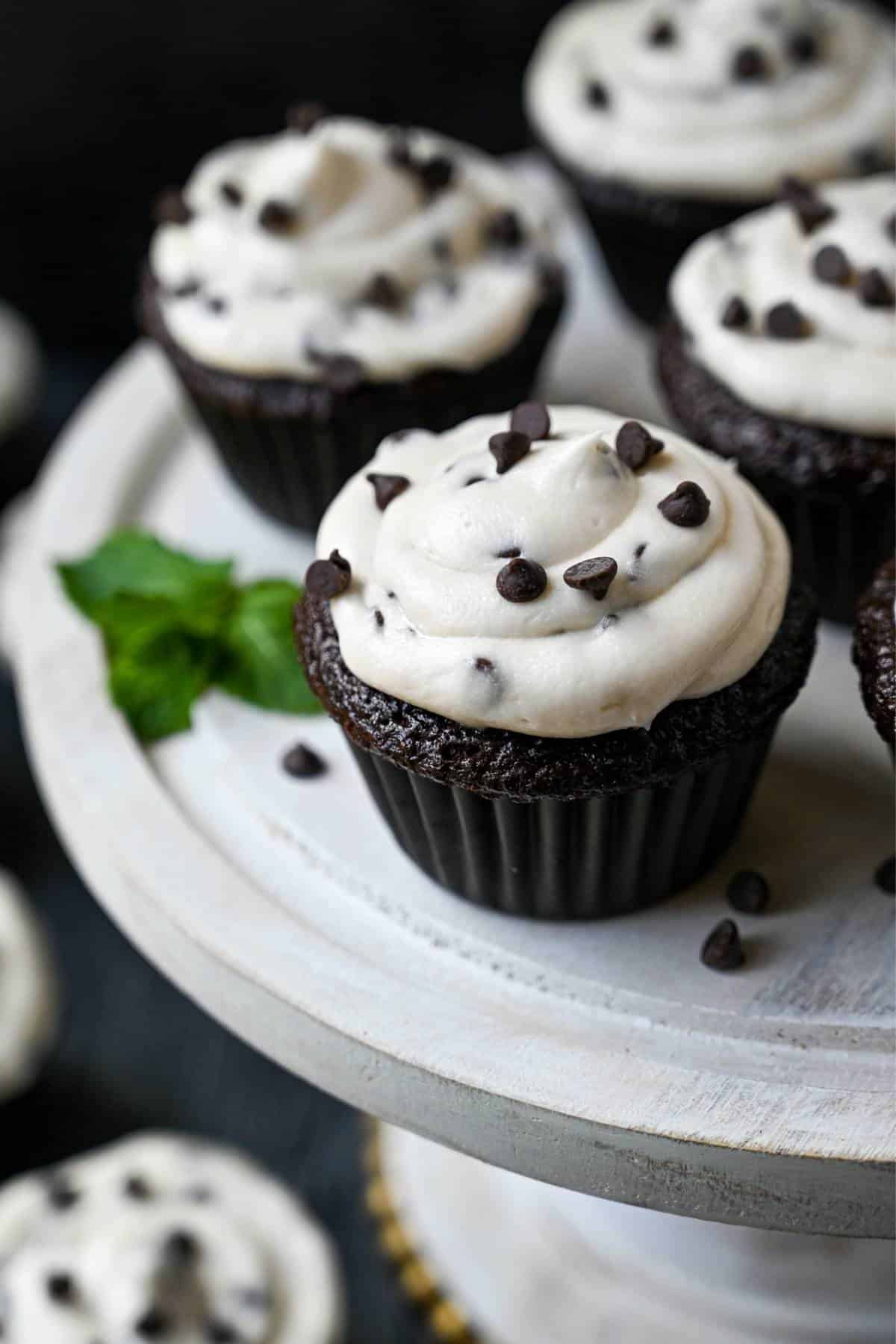 chocolate cupcakes on a white platter topped with chocolate chip frosting sprinkled with mini chocolate chips on top
