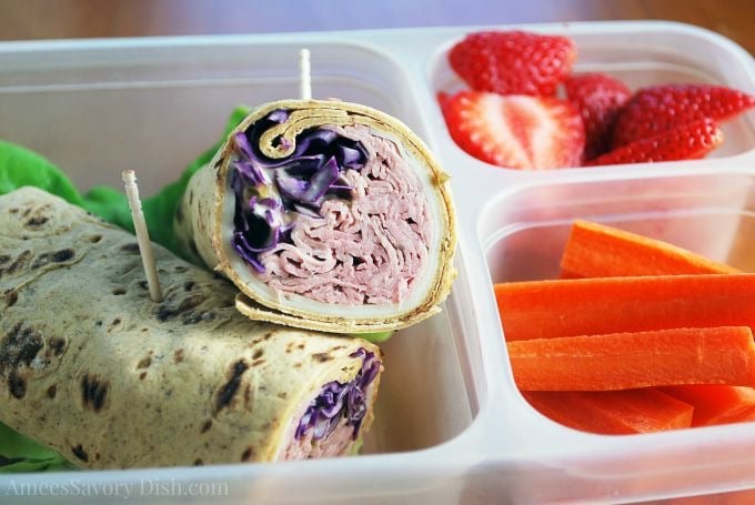 Meal prep container with a Reuben wrap sliced in half, carrots and fresh sliced strawberries