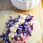 Tortilla wrap topped with roast beef, shredded red cabbage, and thousand island dressing on a cutting board