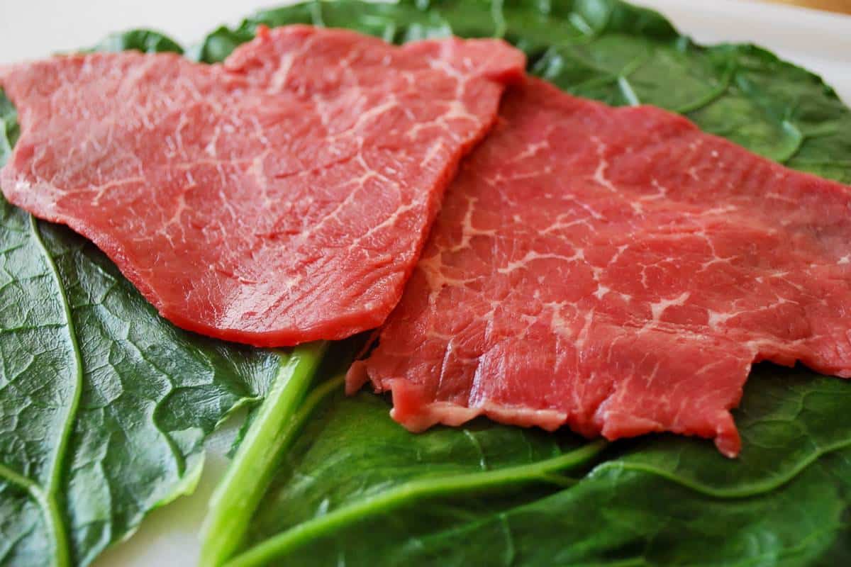 thinly sliced sirloin steak on top of a blanched collard leaf