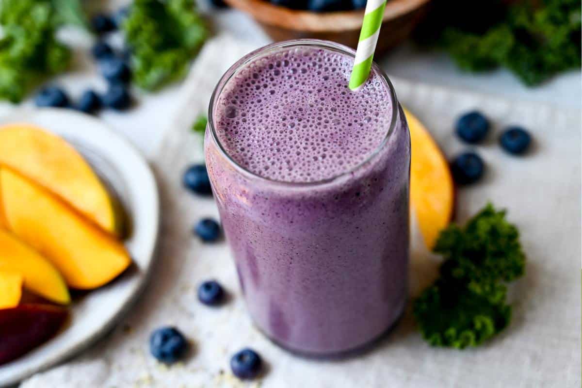 close up of a blueberry smoothie with greens and tropical fruits in a glass 