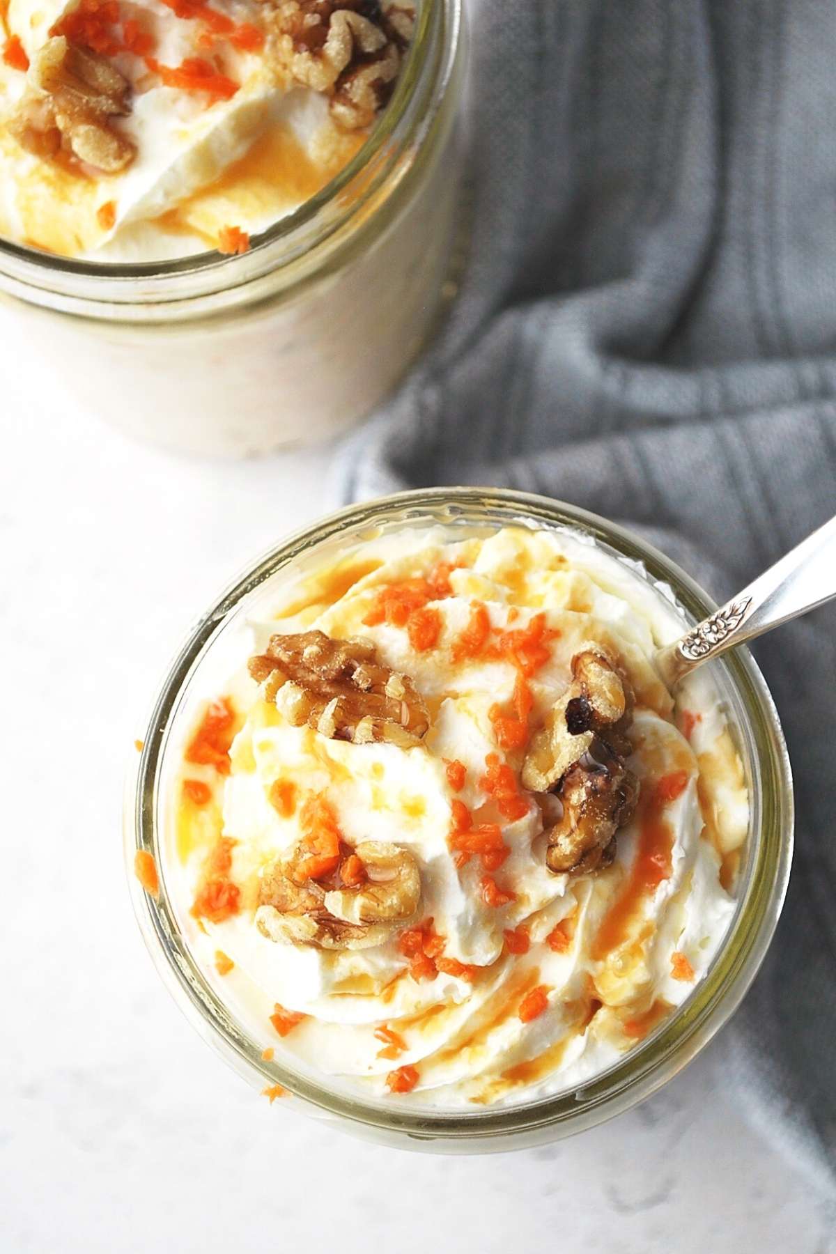 overhead photo of overnight oats in a mason jar topped with whipped cream, nuts, shredded carrots and maple syrup