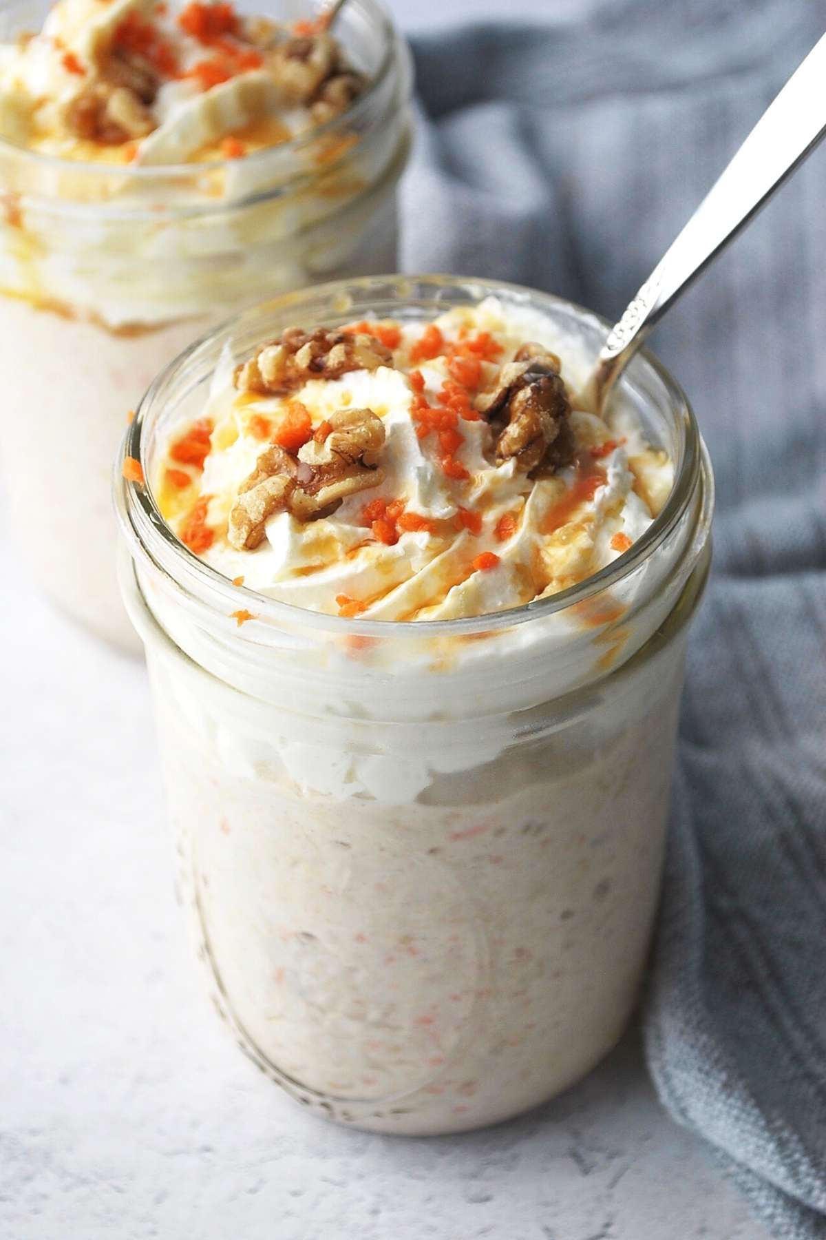 overhead photo of carrot cake oats in two mason jars topped with whipped cream, walnuts, carrots, and syrup