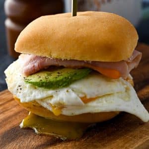 a gluten free breakfast sandwich dripping with yolk on a cutting board
