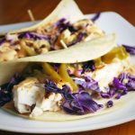 two fish tacos on a plate with purple cabbage and jalapenos