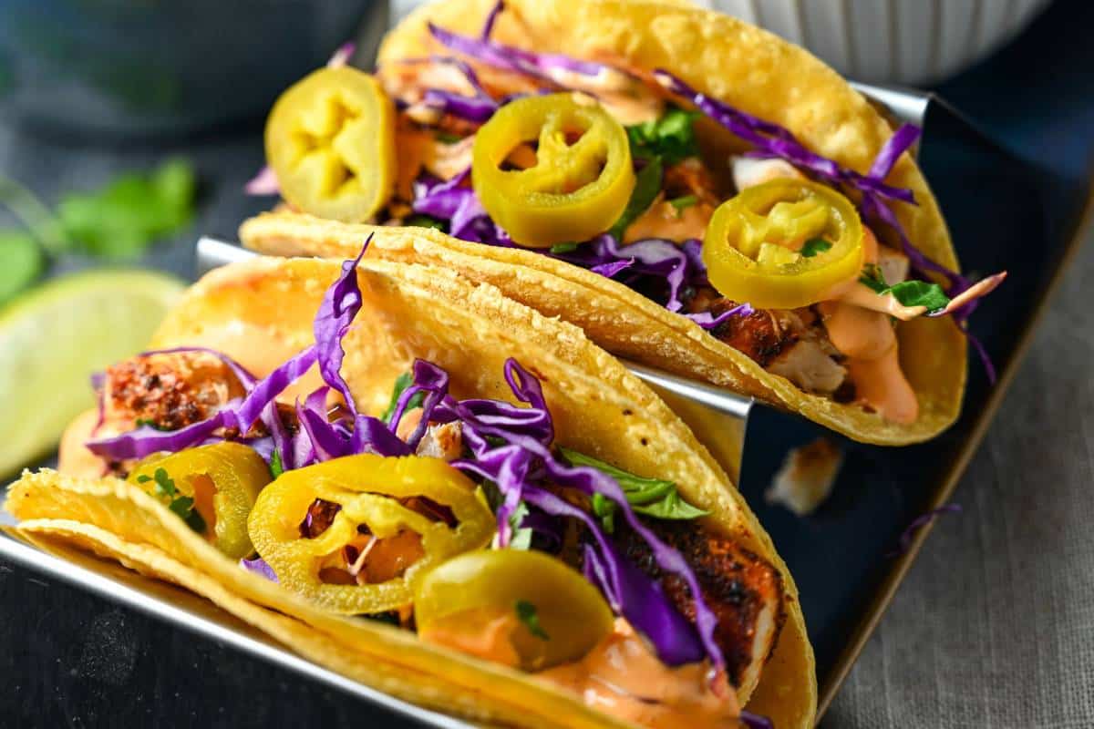 two mahi tacos in a taco holder with chipotle sauce, cabbage, and pickled jalapenos