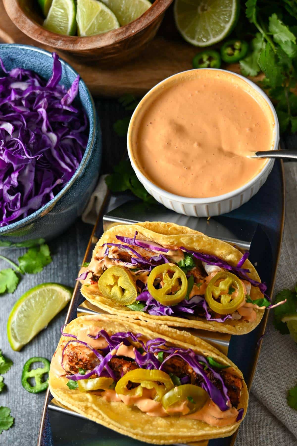 overhead photo of fish tacos with a bowl of chipotle sauce, red cabbage, and a bowl of limes
