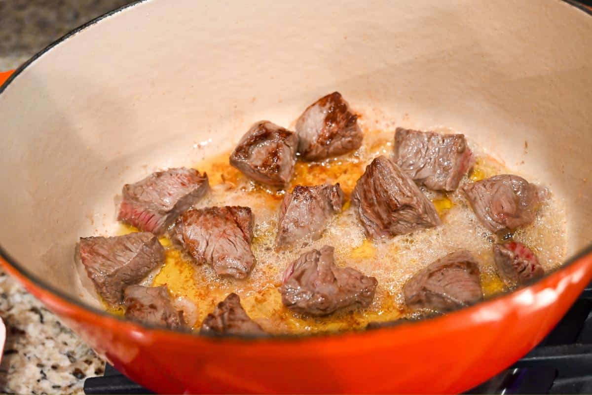 chunks of bottom round roast searing in a dutch oven